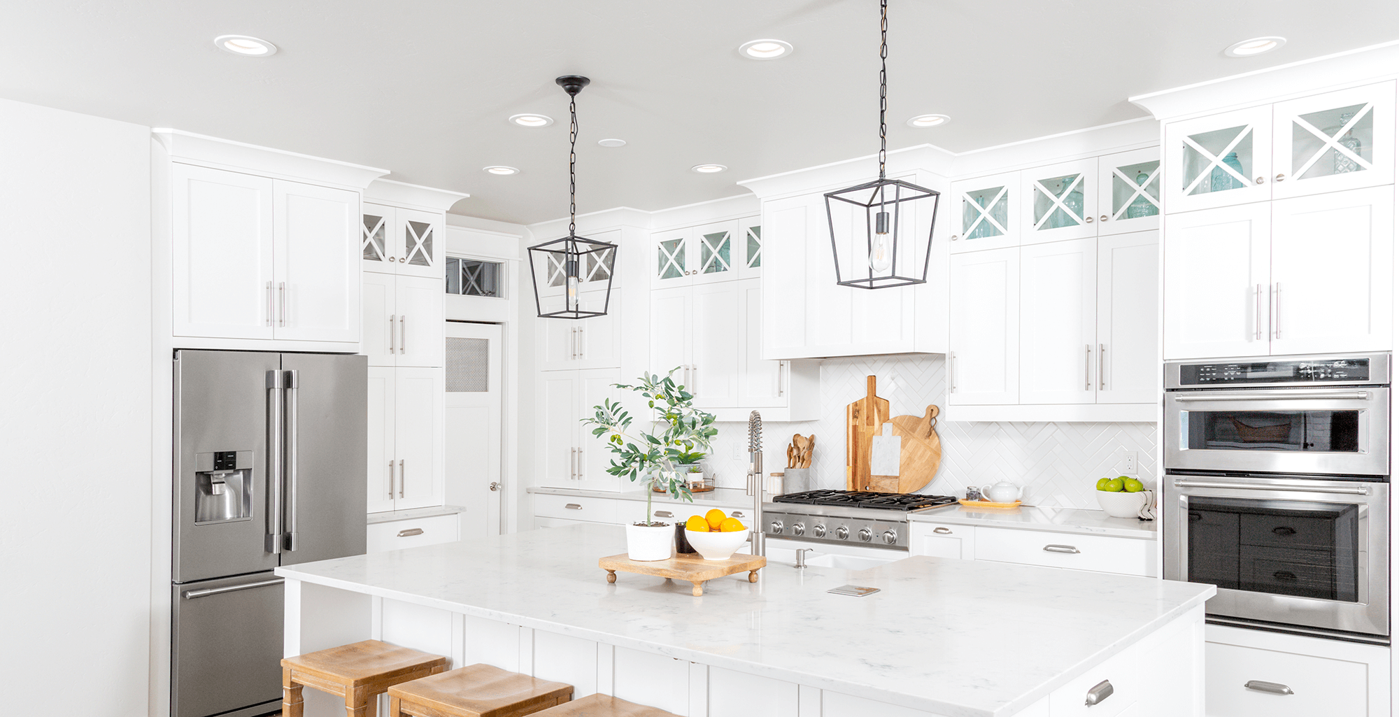 White shaker kitchen with a marble island, pendant lanterns and built-in wall ovens