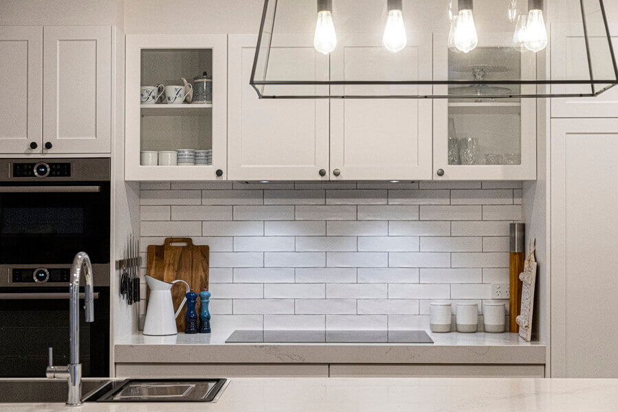 Soft greige shaker kitchen run with glass-front wall cabinets, white brick tile splashback and marble-effect quartz worktop
